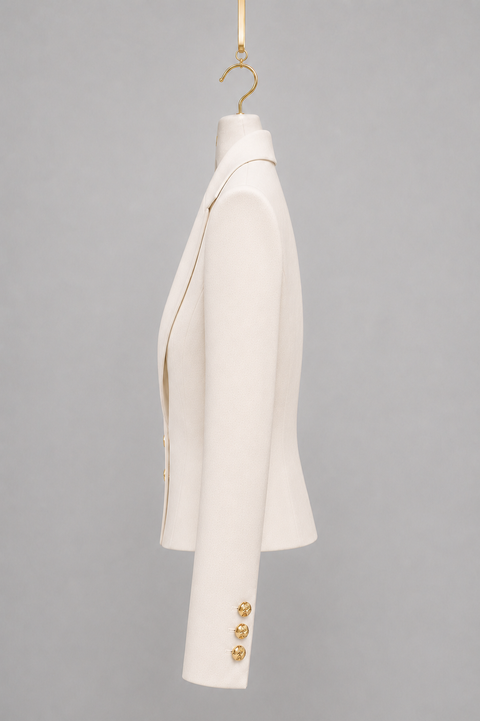 Side view of AURA ivory cropped tailored jacket featuring a sculpted waist, structured shoulder and three gold cuff buttons by Modella