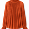 Front view of AURA orange pleated blouse by Modella featuring a ruffled high neckline, fine pleating and flared ruffle cuffs