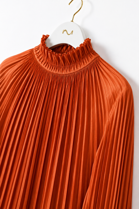 Close-up of AURA orange pleated blouse by Modella showing the fine pleating and ruffled high-neck collar detail