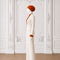 Side view of AURA women’s ivory three-piece tailored suit by Modella with orange pleated blouse, ivory trousers and orange heels
